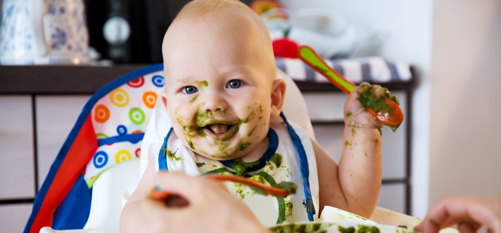 A baby in a high chair is happily eating green food